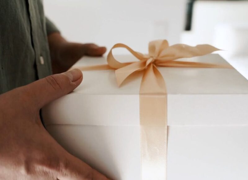 prikaz osobe koja drži poklon u ruci bele boje sa zlatnom mašnicom